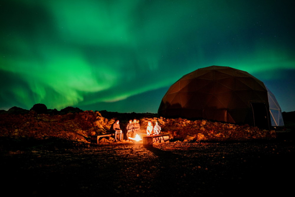 A family sitting by a fire at the Aurora Basecamp, enjoying the northern lights.